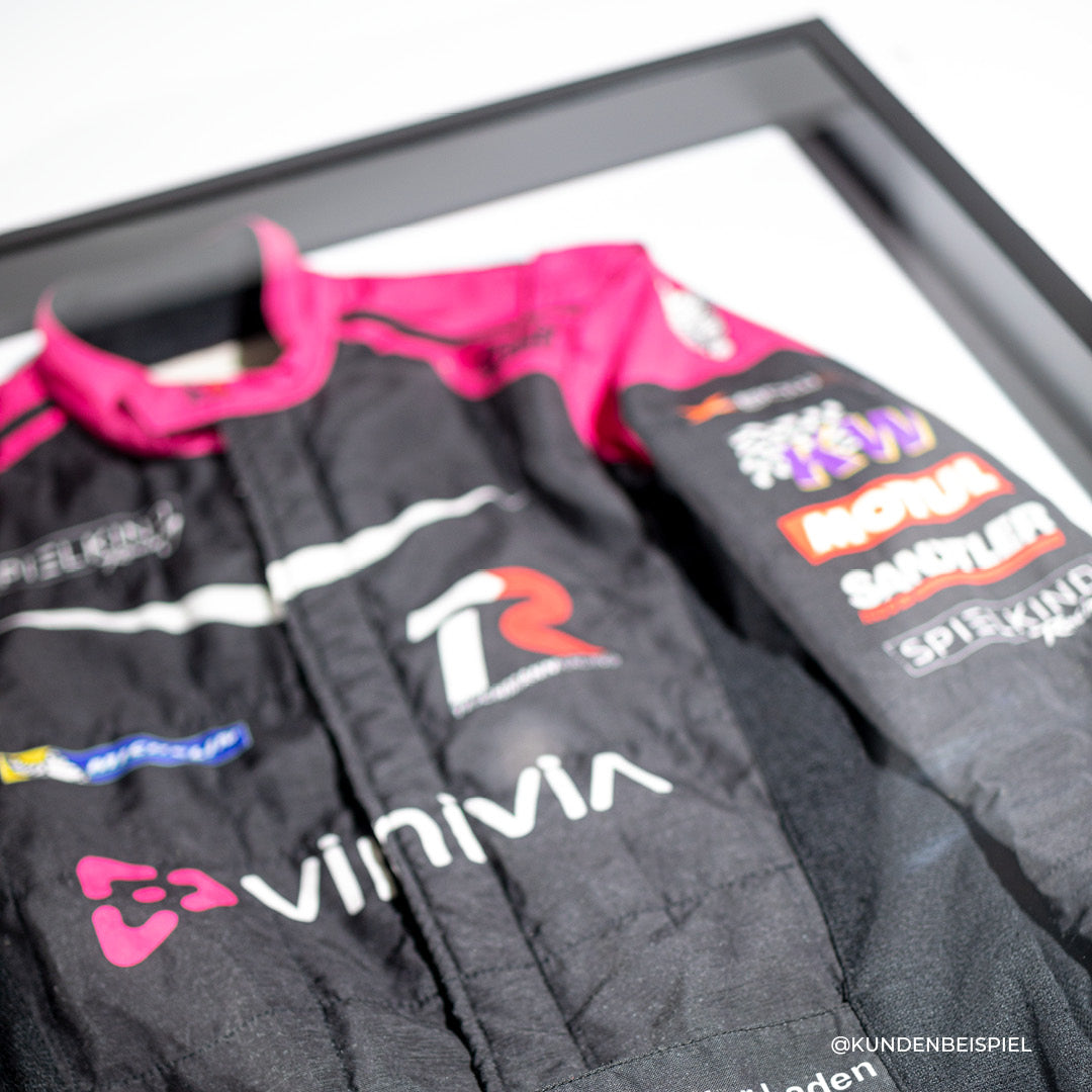 Living.Steel Rennanzugrahmen mit magnetischer Rückwand – schwarz-pinker Anzug inklusive Sponsorenlogos stilvoll präsentiert im hochwertigen Aluminiumrahmen. Kundenbeispiel.