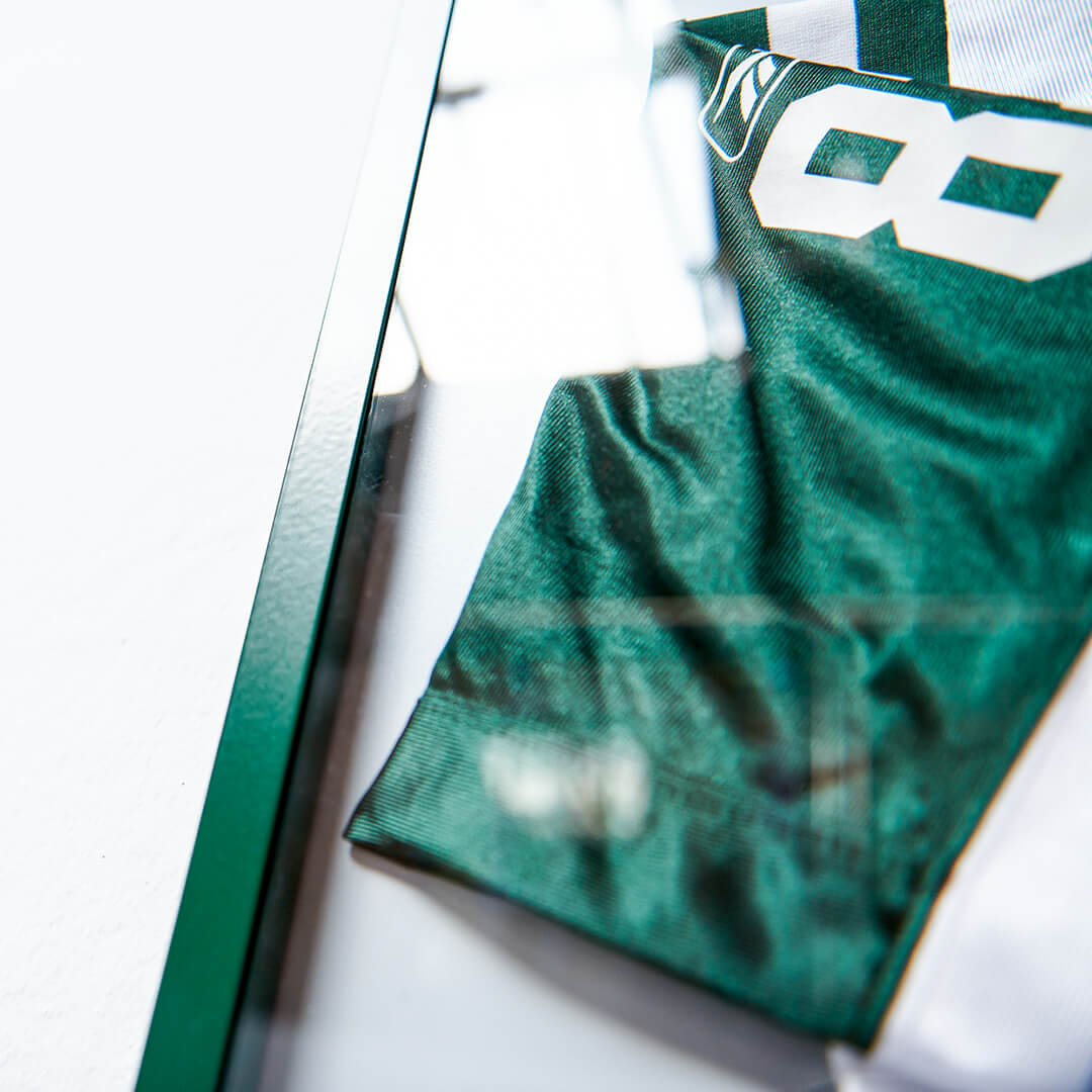 Detailaufnahme eines grünen Living.Steel Rahmens mit Footballtrikot – hochwertiges Aluminiumprofil mit magnetischer Rückwand für sportliche Erinnerungsstücke.